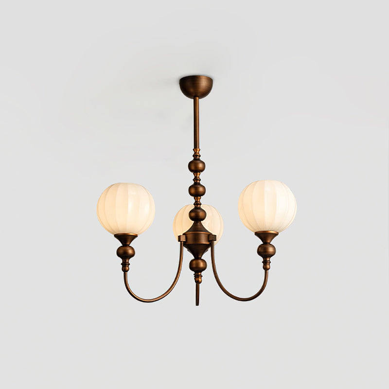 A three-light Clérachic chandelier lit with ribbed globes glowing warm, hung from a short bronze stem against a pale grey ceiling.