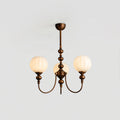 A three-light Clérachic chandelier lit with ribbed globes glowing warm, hung from a short bronze stem against a pale grey ceiling.