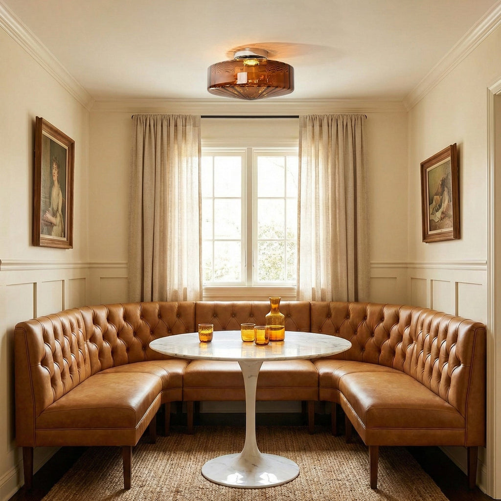 A brown glass Clérachic ceiling light above a round white table and a tan leather banquette, in a room with linen curtains.