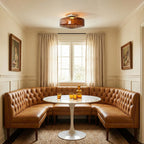 A brown glass Clérachic ceiling light above a round white table and a tan leather banquette, in a room with linen curtains.