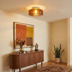 A lit brown glass Clérachic ceiling light above a curved walnut sideboard, with a dried-flower vase and a potted plant nearby.