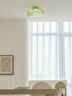 Green ribbed glass Clérachic ceiling light on a white ceiling, with sheer curtains and a framed line drawing below.