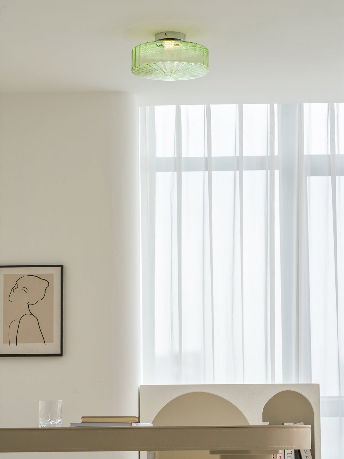 Green ribbed glass Clérachic ceiling light on a white ceiling, with sheer curtains and a framed line drawing below.
