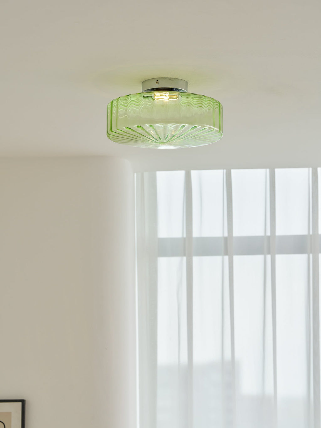 Closer view of this Clérachic ceiling light in green ribbed glass, lit on a white ceiling above sheer curtains.