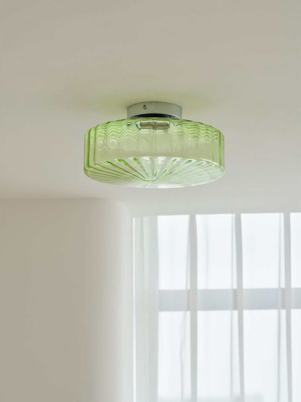 Underside of this Clérachic ceiling light, its green glass ribs radiating out, with sheer windows in the background.