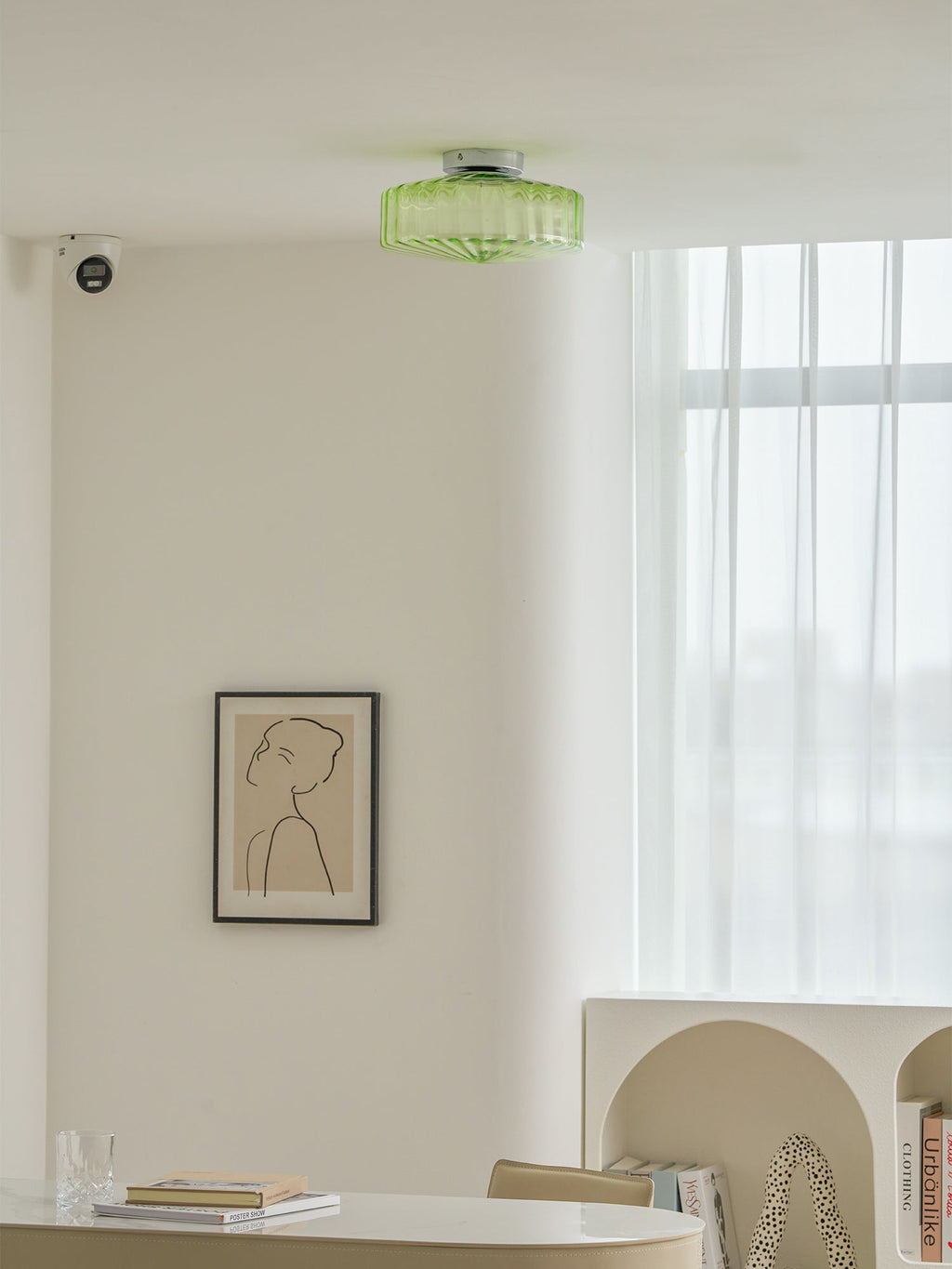 Distant view of a green Clérachic ceiling light high on a white ceiling, above a framed print and a desk.