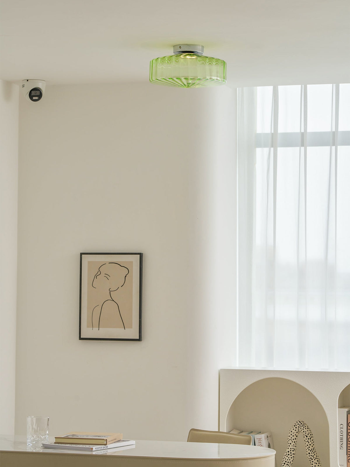 This Clérachic ceiling light in green glass on a white ceiling, with a framed line drawing and a long window below.