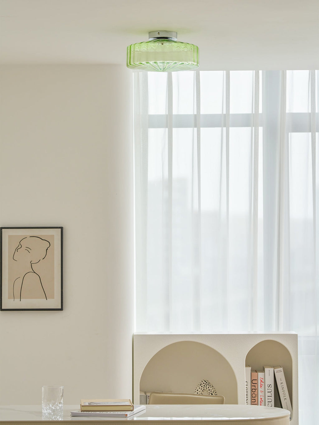 Green Clérachic ceiling light above a room with a framed drawing, sheer curtains and a table with an arched shelf.