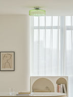 Green Clérachic ceiling light above a room with a framed drawing, sheer curtains and a table with an arched shelf.