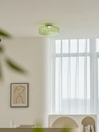 A green ribbed glass Clérachic ceiling light with a blurred leaf in the foreground, above a window and a framed print.