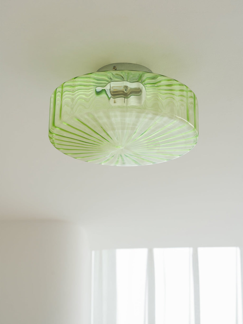 Green Clérachic ceiling light seen from below on a white ceiling, with fine ribs radiating across the glass.