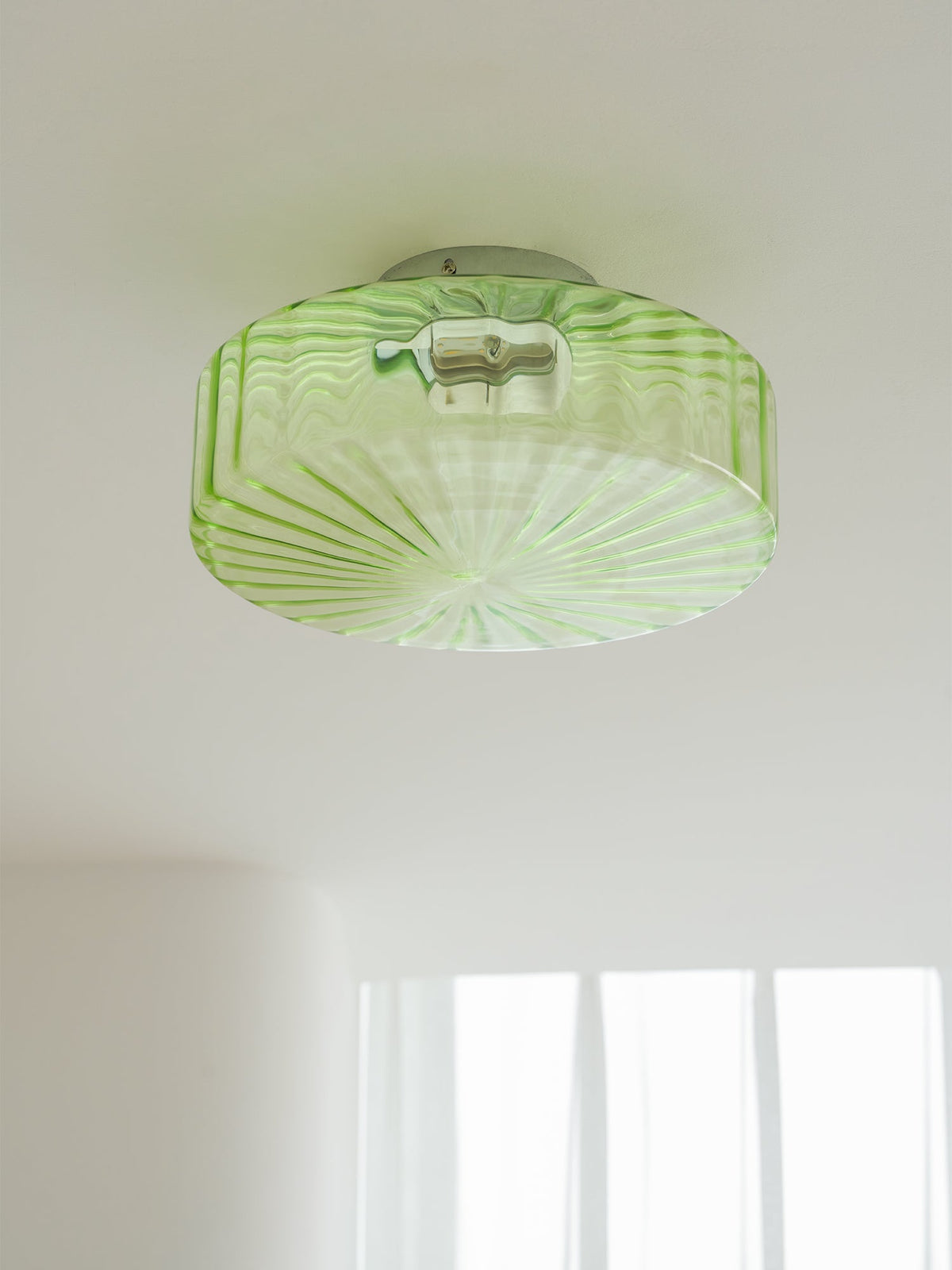 Green Clérachic ceiling light seen from below on a white ceiling, with fine ribs radiating across the glass.