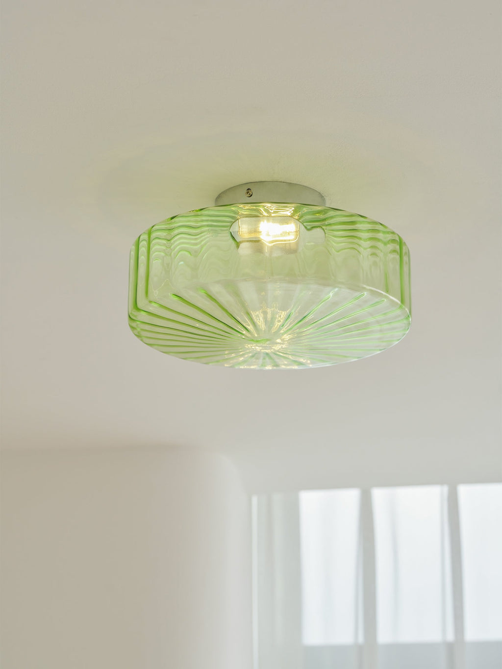 This Clérachic ceiling light in green ribbed glass lit on a white ceiling, with a faint soft shadow around it.