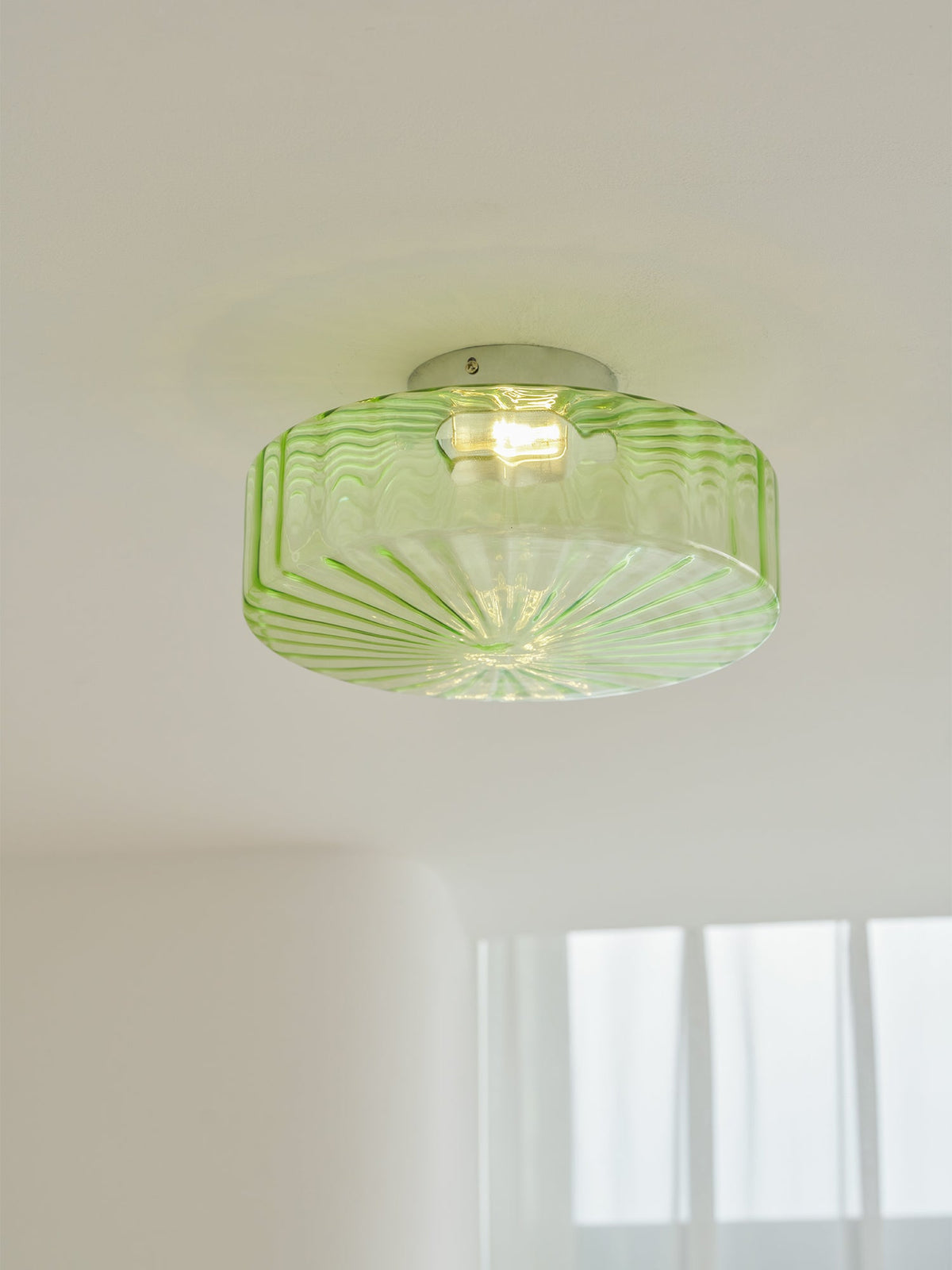 This Clérachic ceiling light in green ribbed glass lit on a white ceiling, with a faint soft shadow around it.