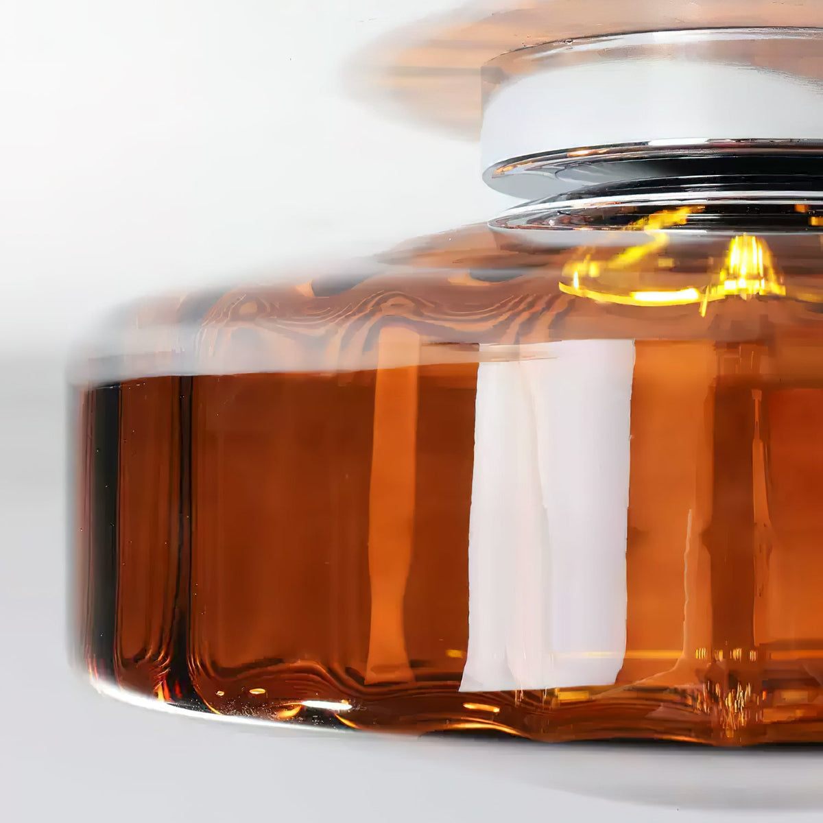 Close view of the amber-brown glass and chrome plate on this Clérachic ceiling light, with a bright bulb inside.