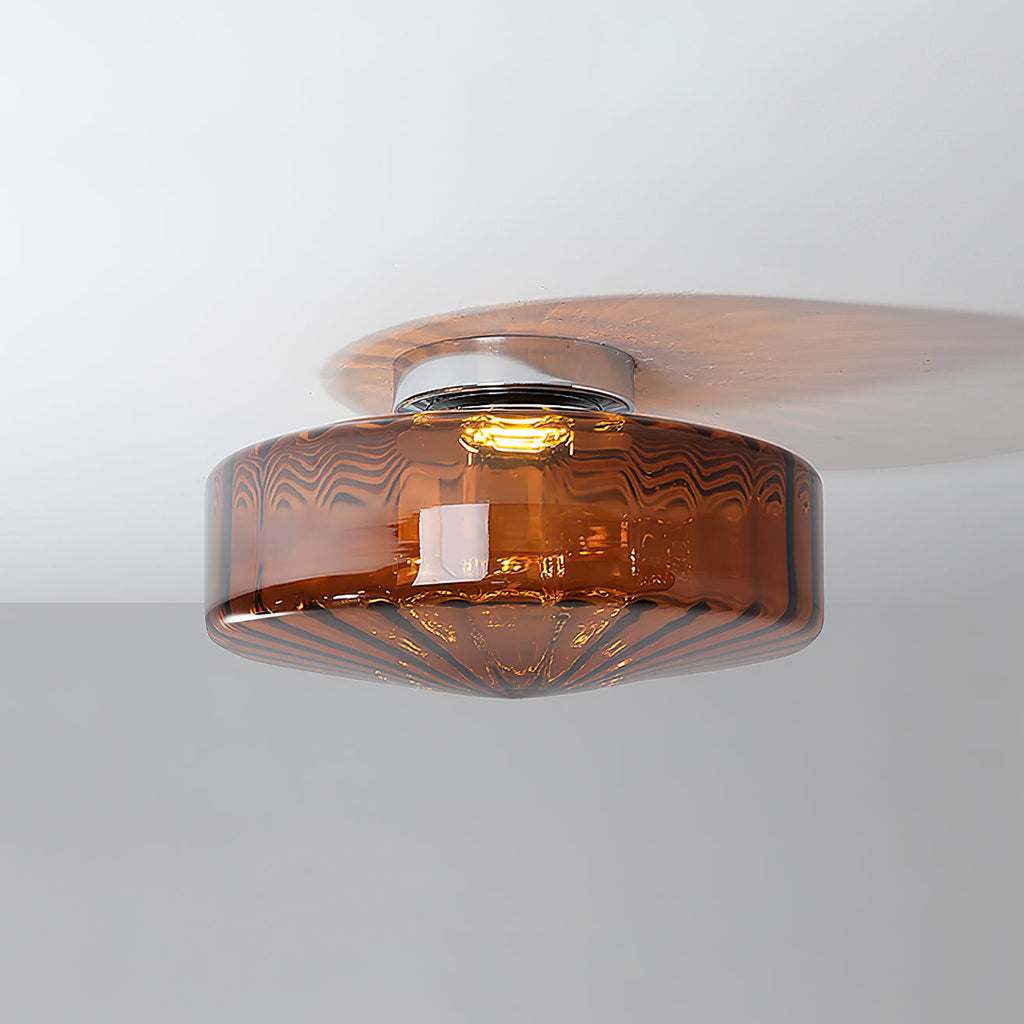 Brown glass Clérachic ceiling light lit from within, with a warm glow and a soft shadow across the ceiling.
