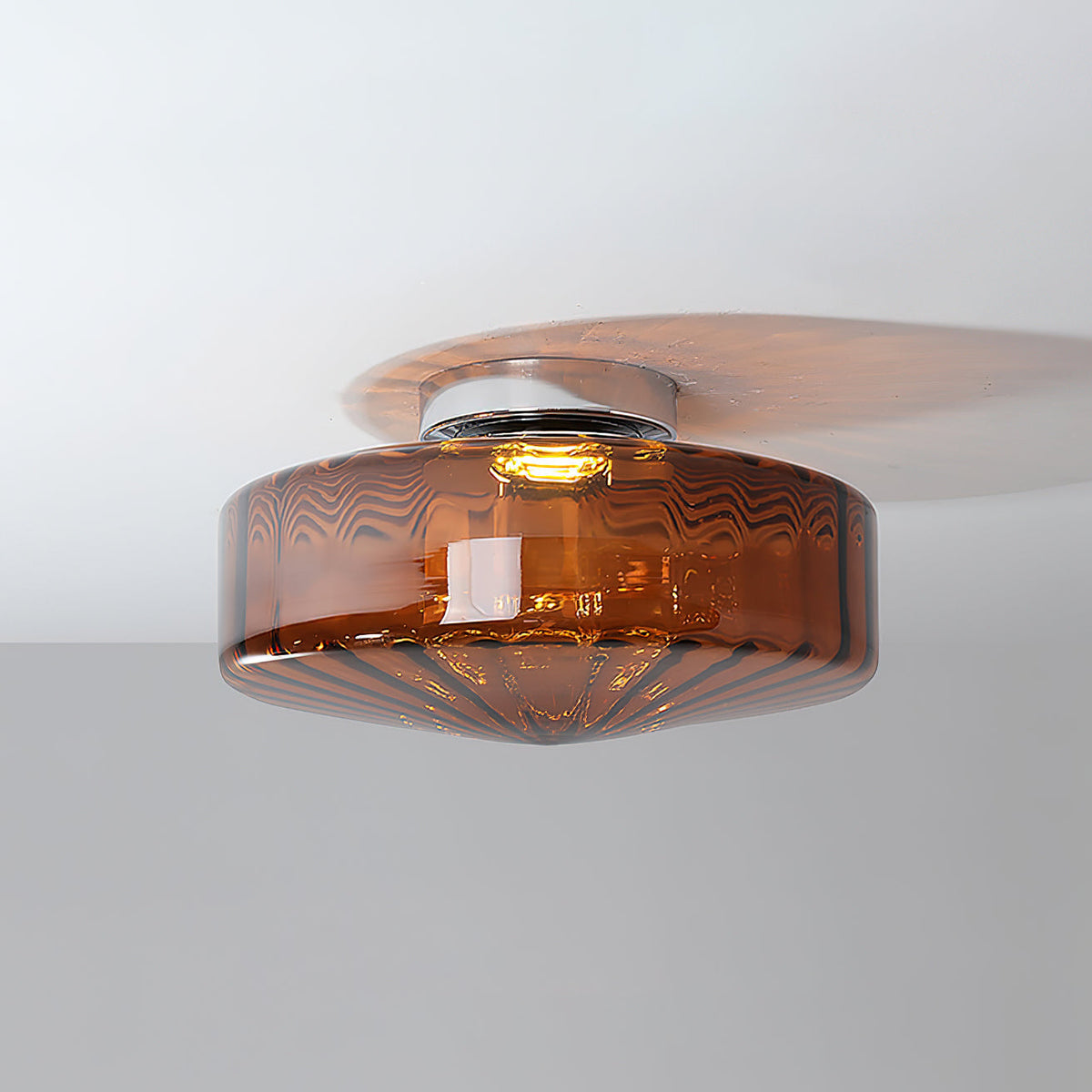 Brown glass Clérachic ceiling light lit from within, with a warm glow and a soft shadow across the ceiling.