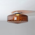 Brown glass Clérachic ceiling light seen from a low side angle, with its chrome plate and a warm glow under the shade.