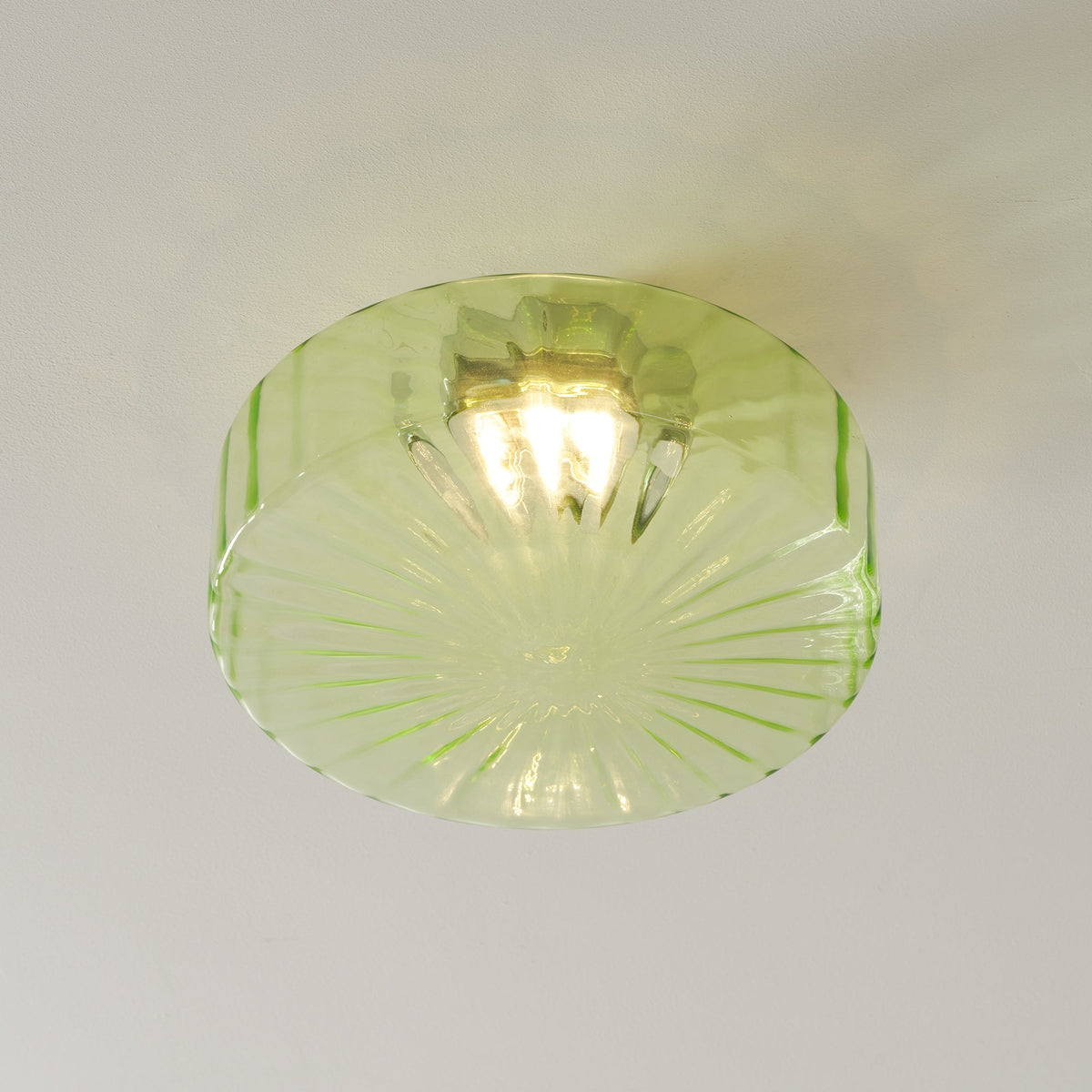 Close view of the green ribbed glass shade on this Clérachic ceiling light, with its bulb glowing inside.