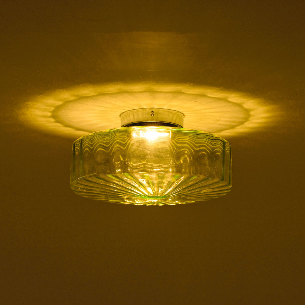 This Clérachic ceiling light lit in a dark room, with a warm yellow glow and a pattern of ribs cast on the ceiling.