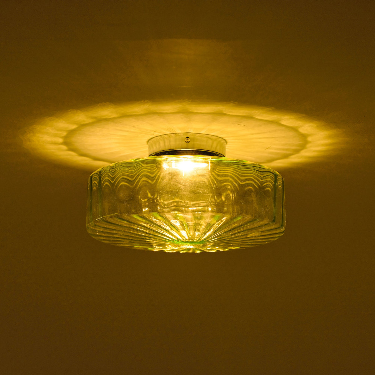 This Clérachic ceiling light lit in a dark room, with a warm yellow glow and a pattern of ribs cast on the ceiling.