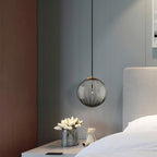 Smoke grey Clérachic glass pendant beside a bed, over a white bedside table with tulips and a toy bear.