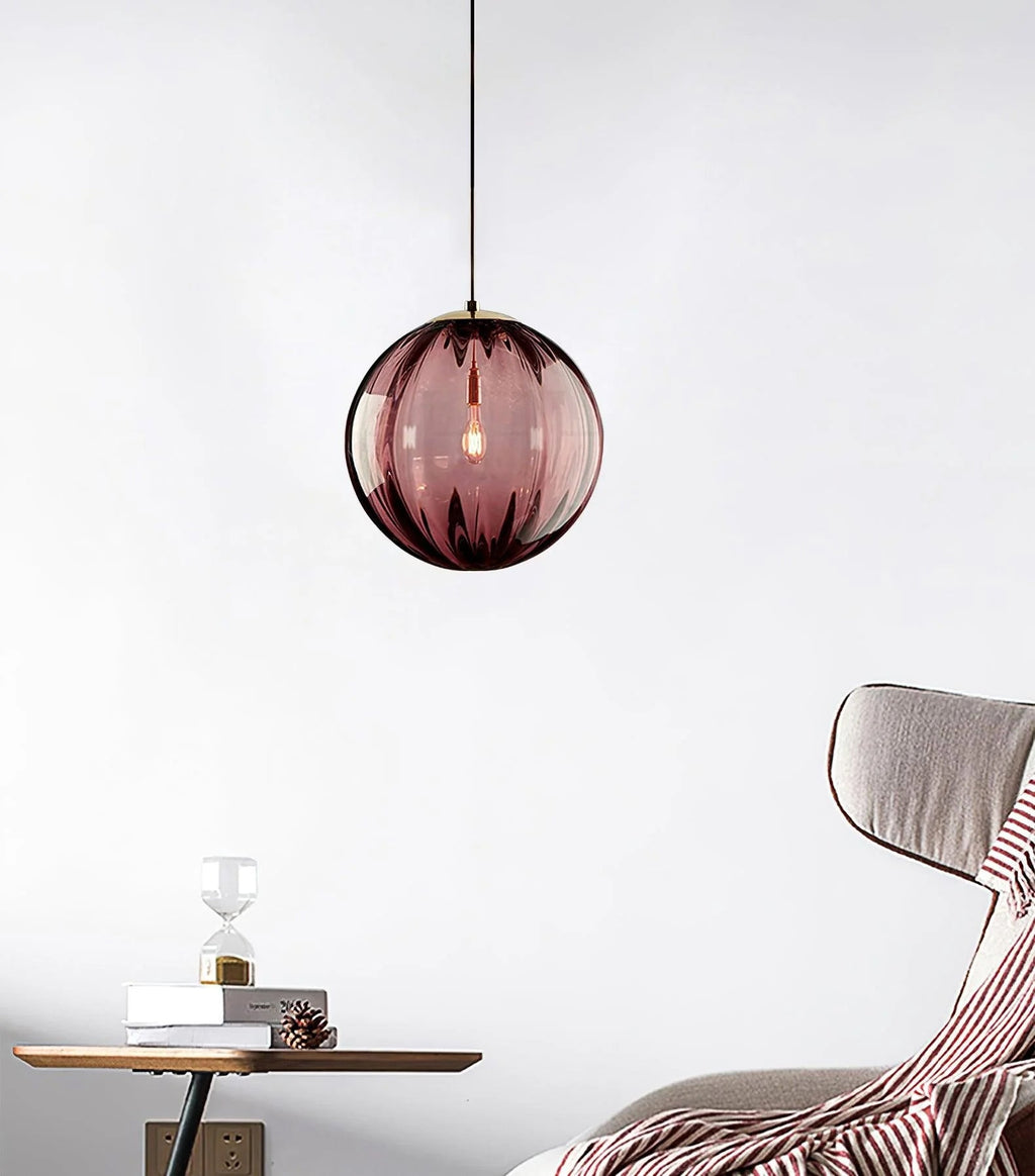 Wine red Clérachic glass pendant hanging by a cord in a pale room, with a striped throw and side table below.