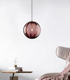Wine red Clérachic glass pendant hanging by a cord in a pale room, with a striped throw and side table below.