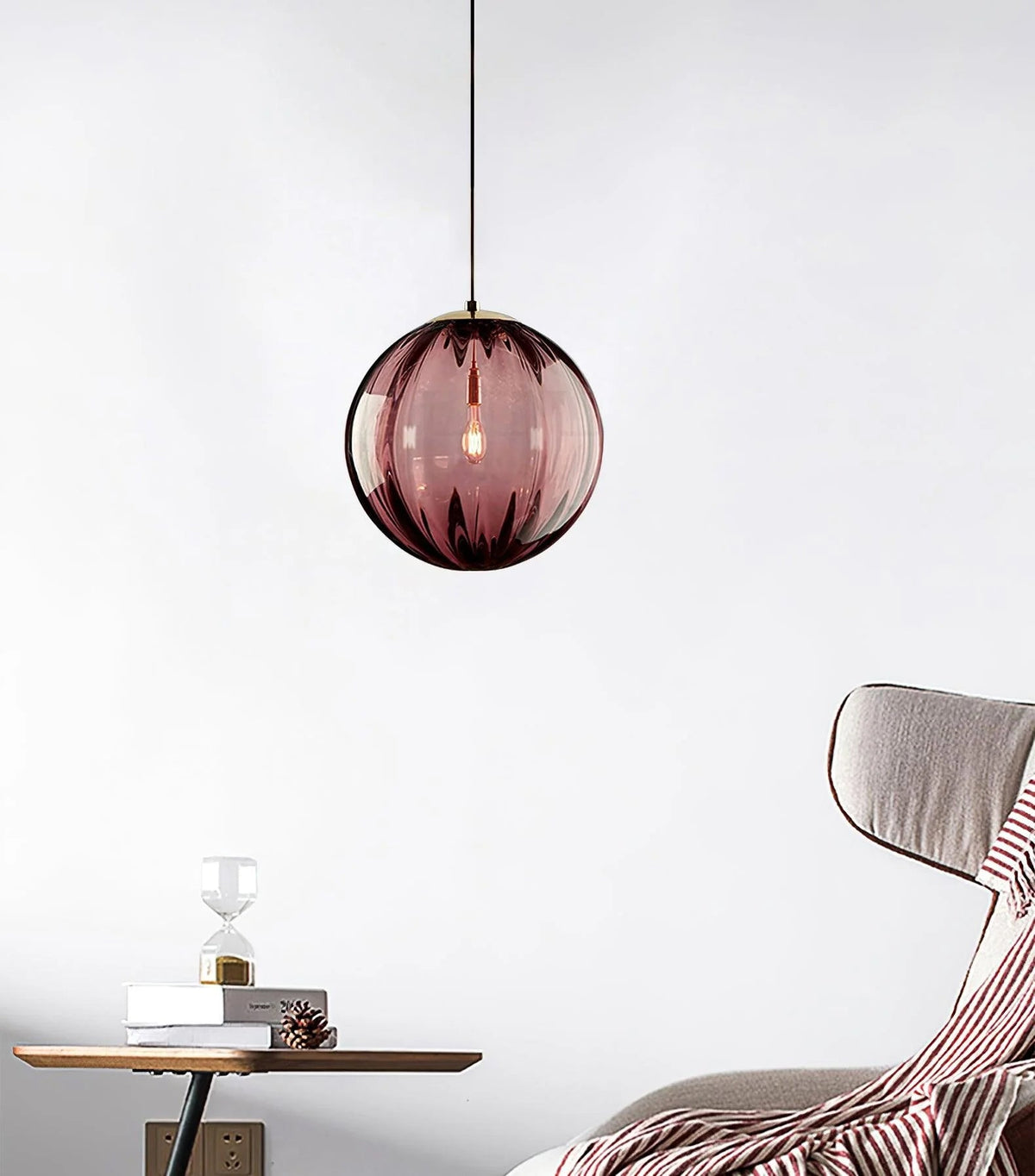 Wine red Clérachic glass pendant hanging by a cord in a pale room, with a striped throw and side table below.