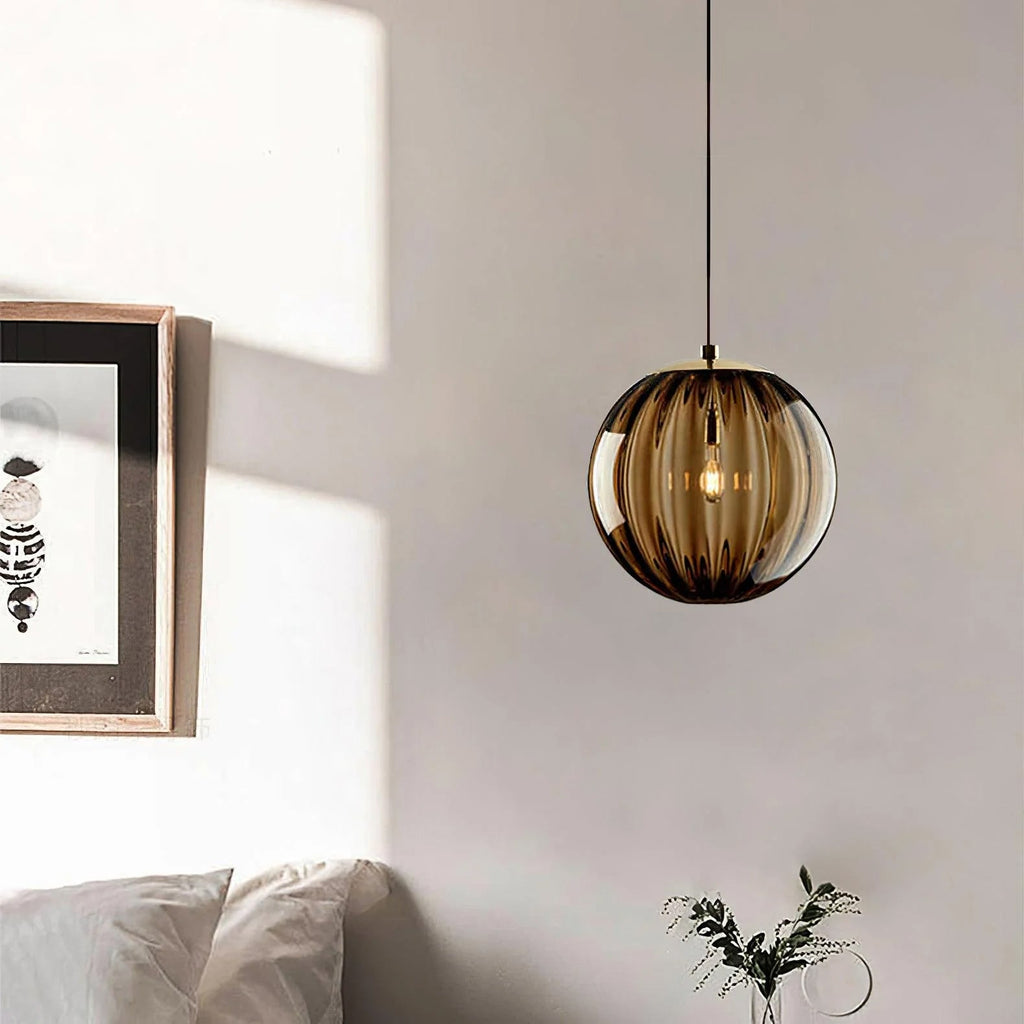 Amber-toned ribbed glass Clérachic pendant beside a framed print, with bedding and a plant sprig below.