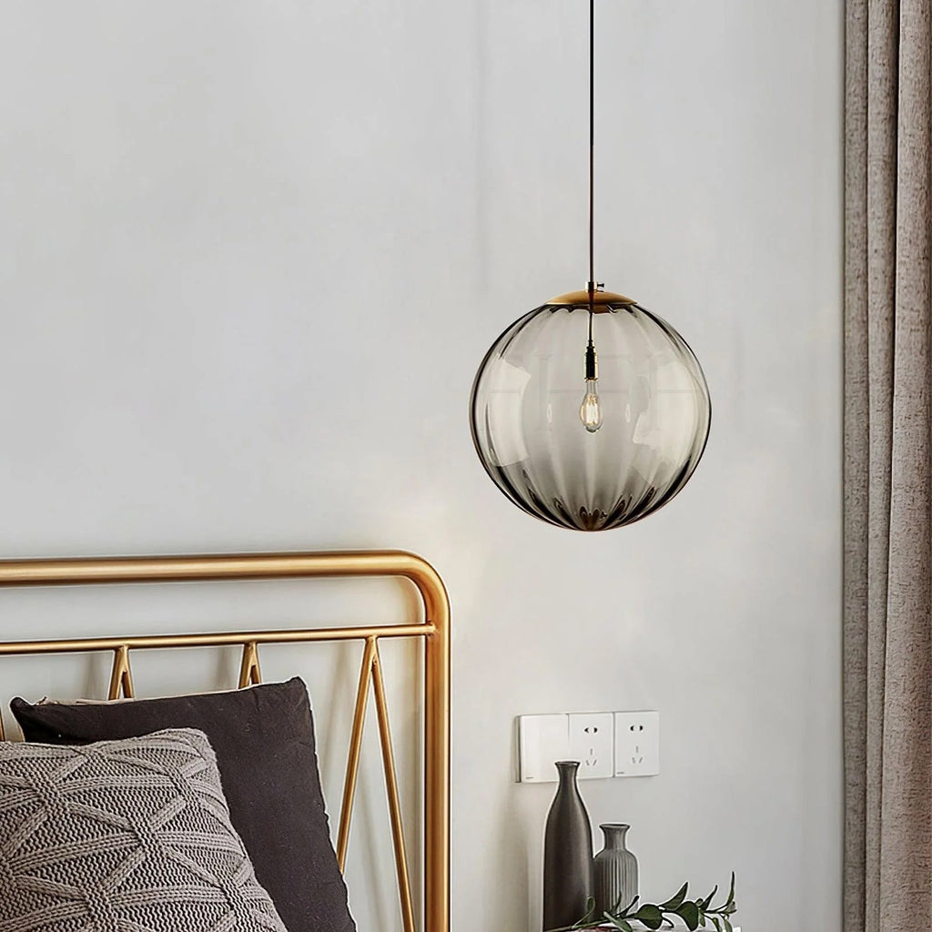 Smoke grey Clérachic pendant with a bronze cap, hanging by a gold bed frame in a pale bedroom.