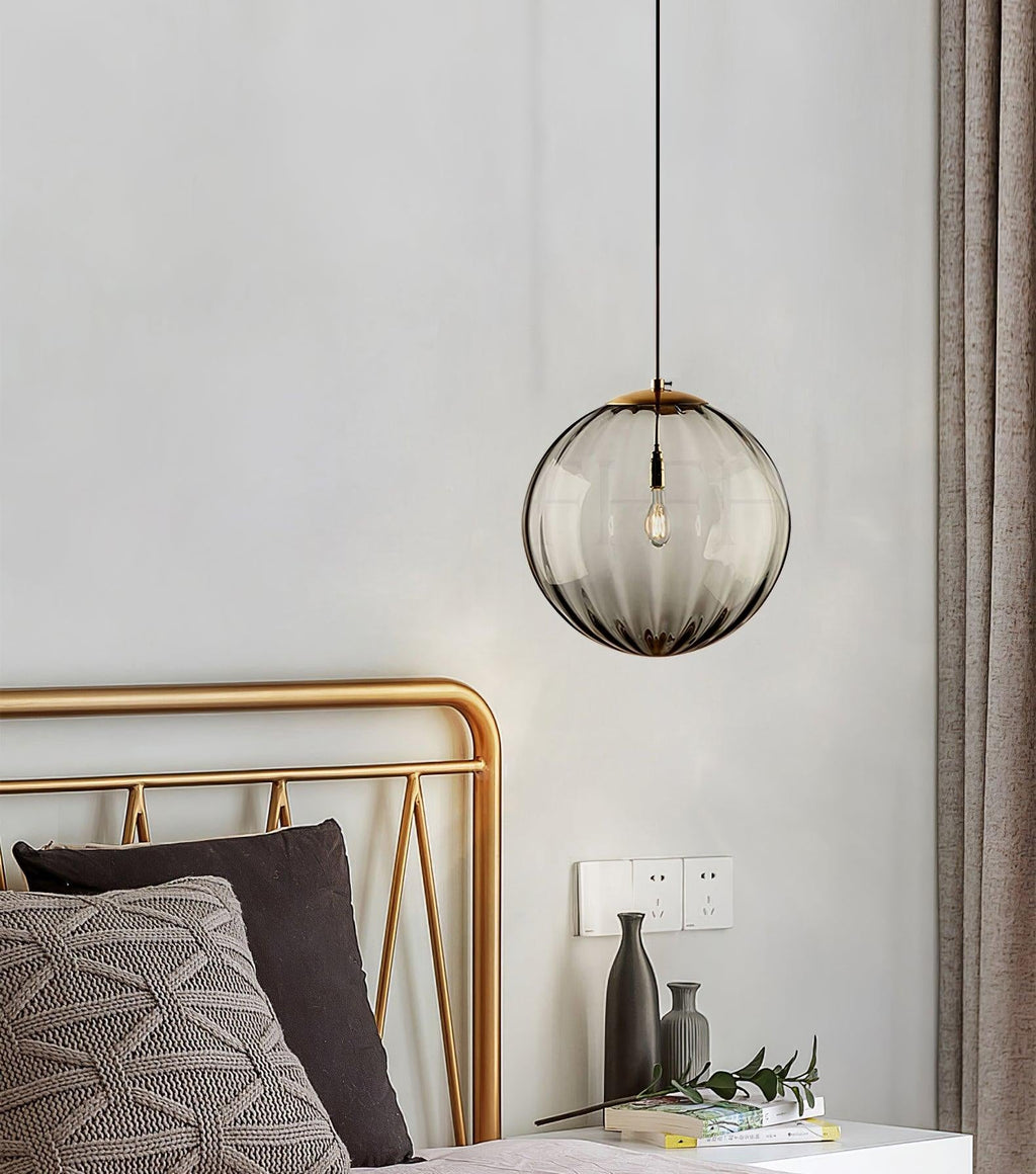 Smoke grey ribbed glass Clérachic pendant hung close to a gold bed frame and a beige curtain.