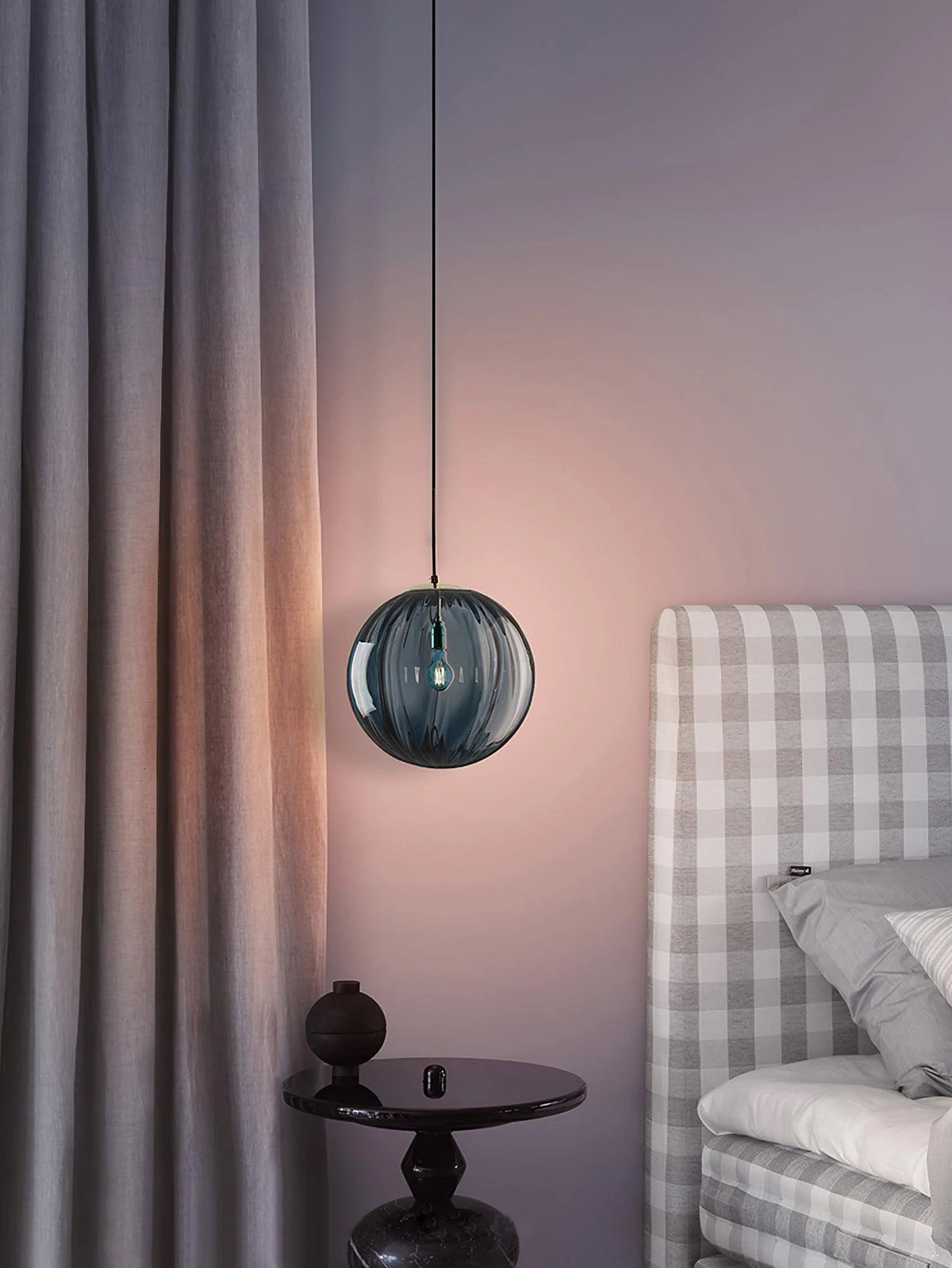 Blue-grey Clérachic glass pendant lit beside a lavender wall, with a grey curtain and a checked headboard.
