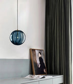 Blue ribbed glass Clérachic pendant above a white sideboard, with a framed portrait leaning below.