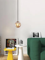 Small amber Clérachic glass pendant in a white room with a green sofa, a yellow stool and framed art.