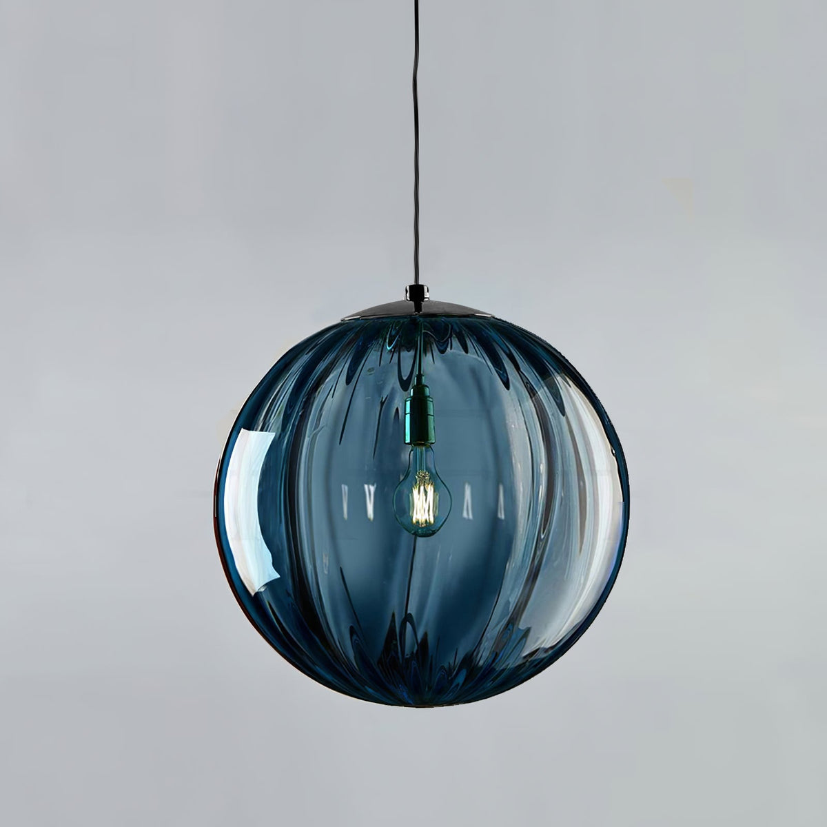 Large blue Clérachic glass globe with vertical ribs and a black cap, a bulb lit inside on a grey backdrop.