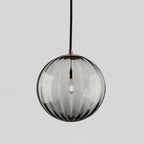 Smoke grey ribbed glass Clérachic pendant with a gold-toned cap, an unlit bulb visible inside.