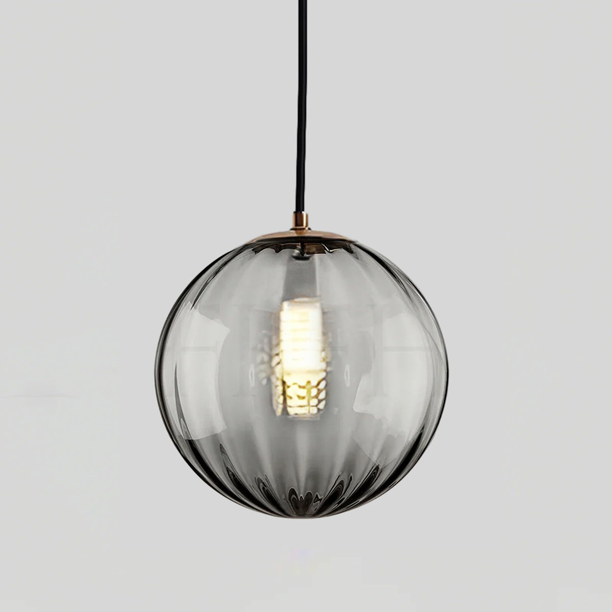 Smaller smoke grey Clérachic glass pendant with a gold-toned cap and a lit bulb inside.