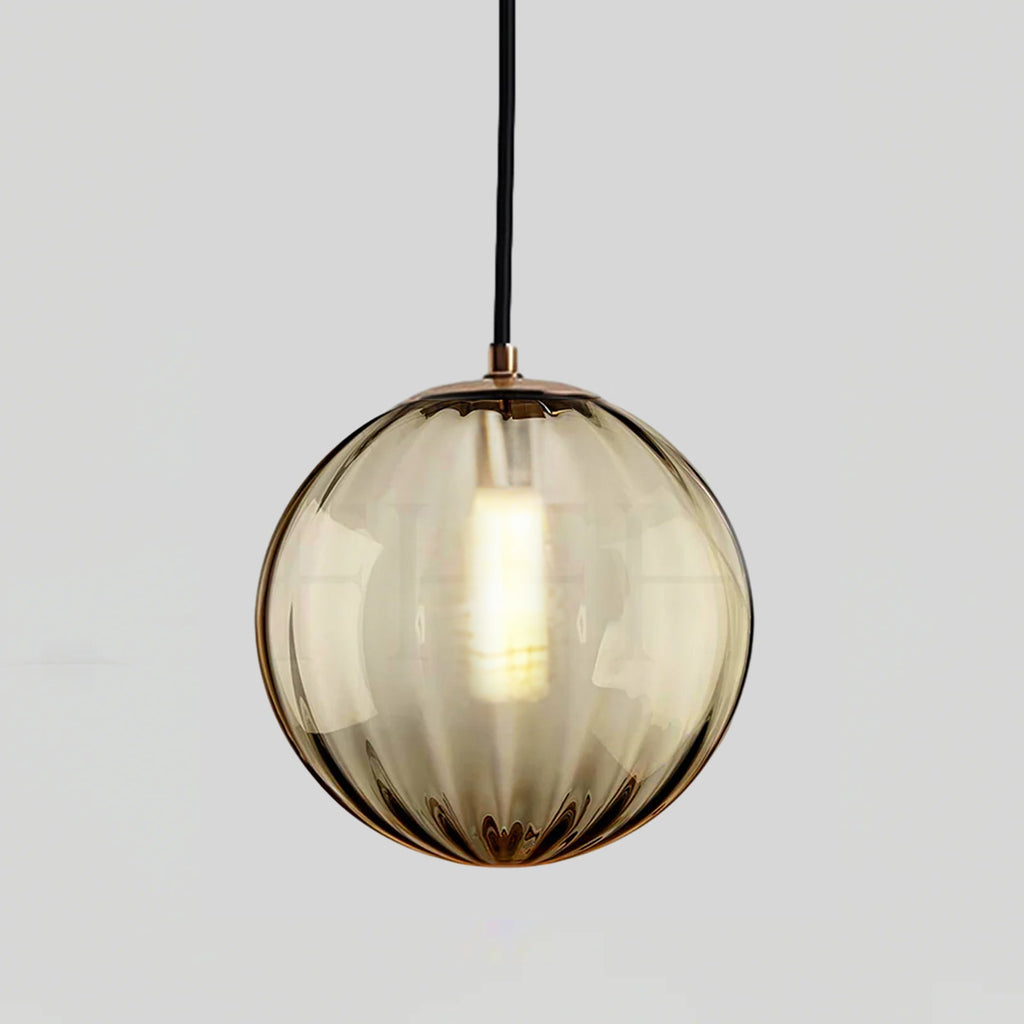 Smaller amber Clérachic glass pendant with a gold-toned cap and a lit bulb, on light grey.
