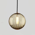 Smaller amber Clérachic glass pendant with a gold-toned cap and a lit bulb, on light grey.