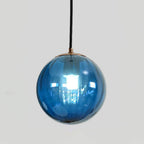 Blue Clérachic glass globe pendant with a gold-toned cap, a bright bulb showing through the glass.