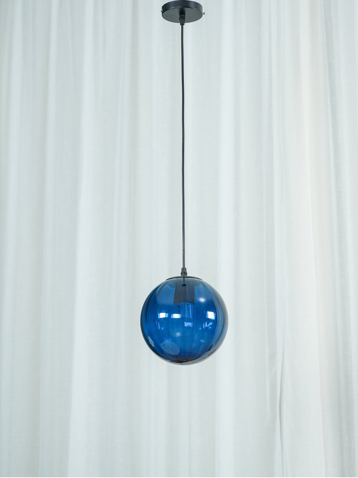Compact blue Clérachic glass pendant hung high in front of a white curtain, black ceiling canopy above.