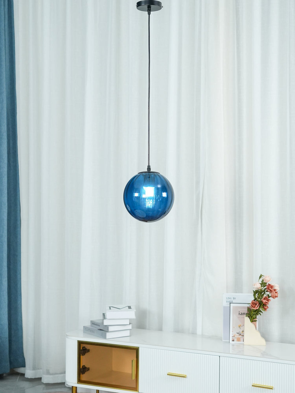 Blue Clérachic glass pendant hanging at mid-height by curtains, with a white sideboard in the corner.