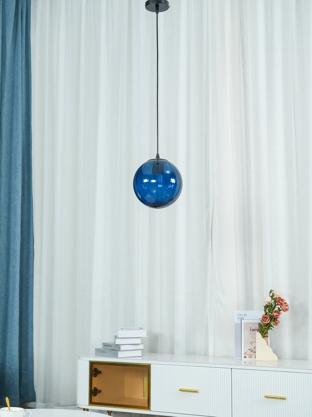 Blue Clérachic glass pendant just below its black canopy, with a curtain and sideboard behind.