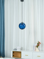 Blue Clérachic glass pendant just below its black canopy, with a curtain and sideboard behind.