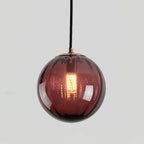 Close view of a wine red Clérachic glass globe with fine vertical ribs and a glowing filament bulb.