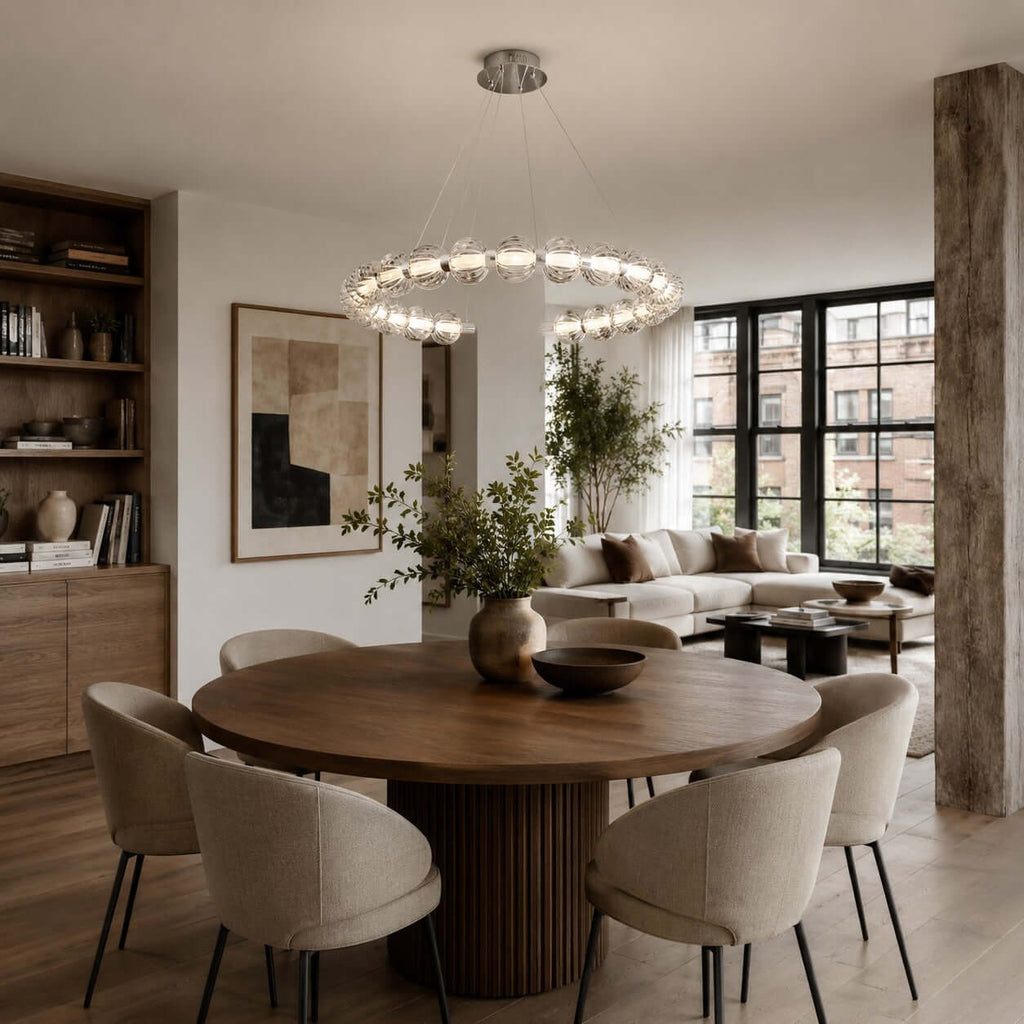A horizontal ring of glass beads hangs over a round walnut dining table with cream chairs, a Clérachic pendant in an open-plan room.