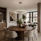 A horizontal ring of glass beads hangs over a round walnut dining table with cream chairs, a Clérachic pendant in an open-plan room.