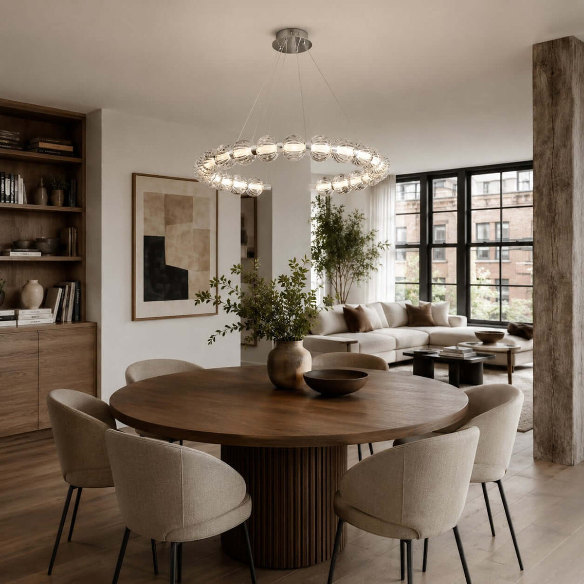 A horizontal ring of glass beads hangs over a round walnut dining table with cream chairs, a Clérachic pendant in an open-plan room.