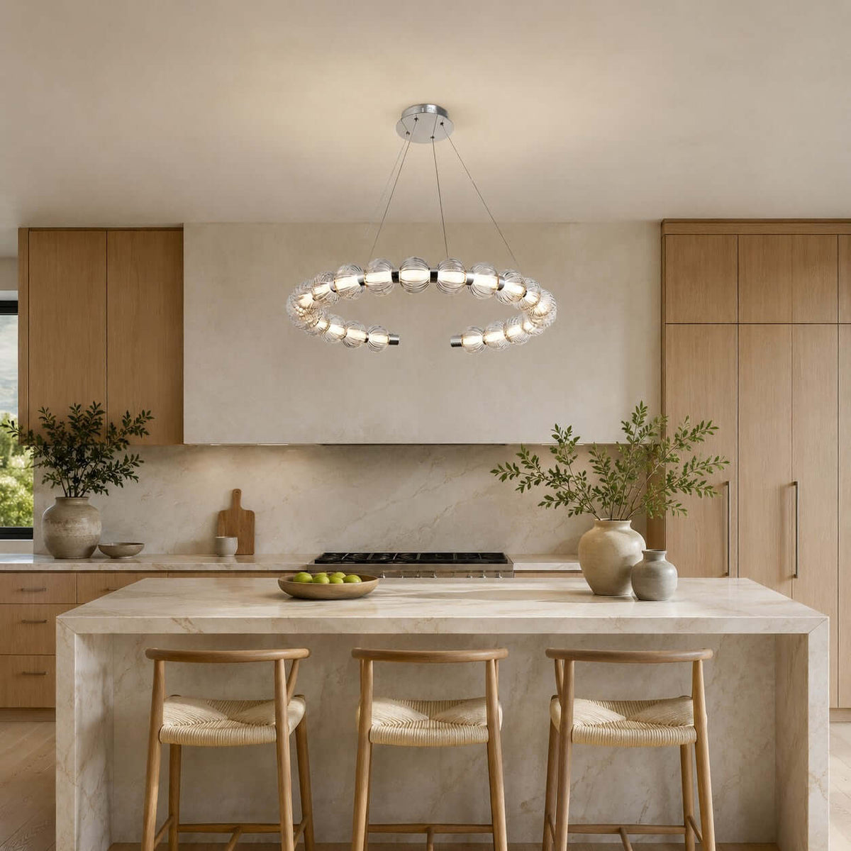 Ring of ribbed glass beads glowing above a travertine-style island with rush-seat stools, a Clérachic pendant in a light oak kitchen.